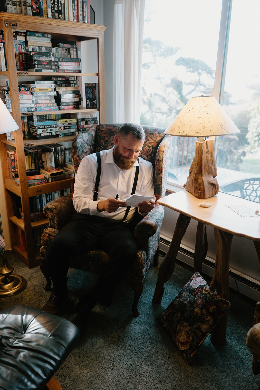 A man sits at a chair near a lamp in a beach Airbnb and writes his vows for his Florence, Oregon elopement.