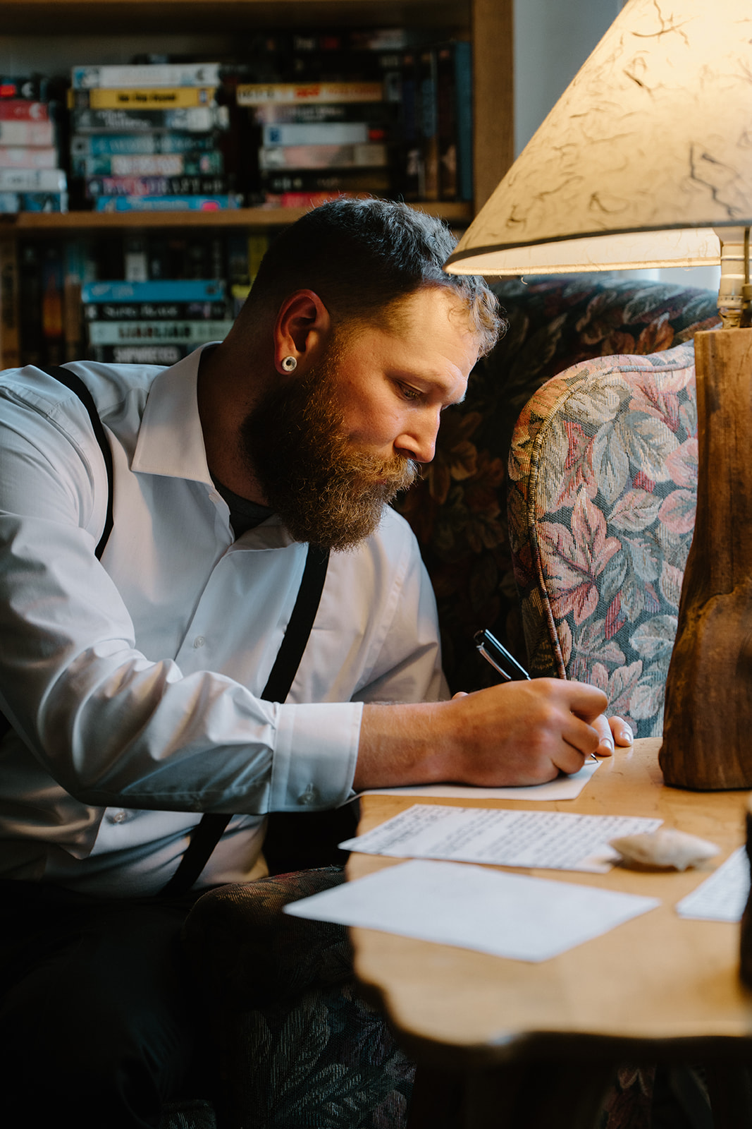 A close up photo of a man sitting at a chair near a lamp in a beach Airbnb and writes his vows for his Florence, Oregon elopement.