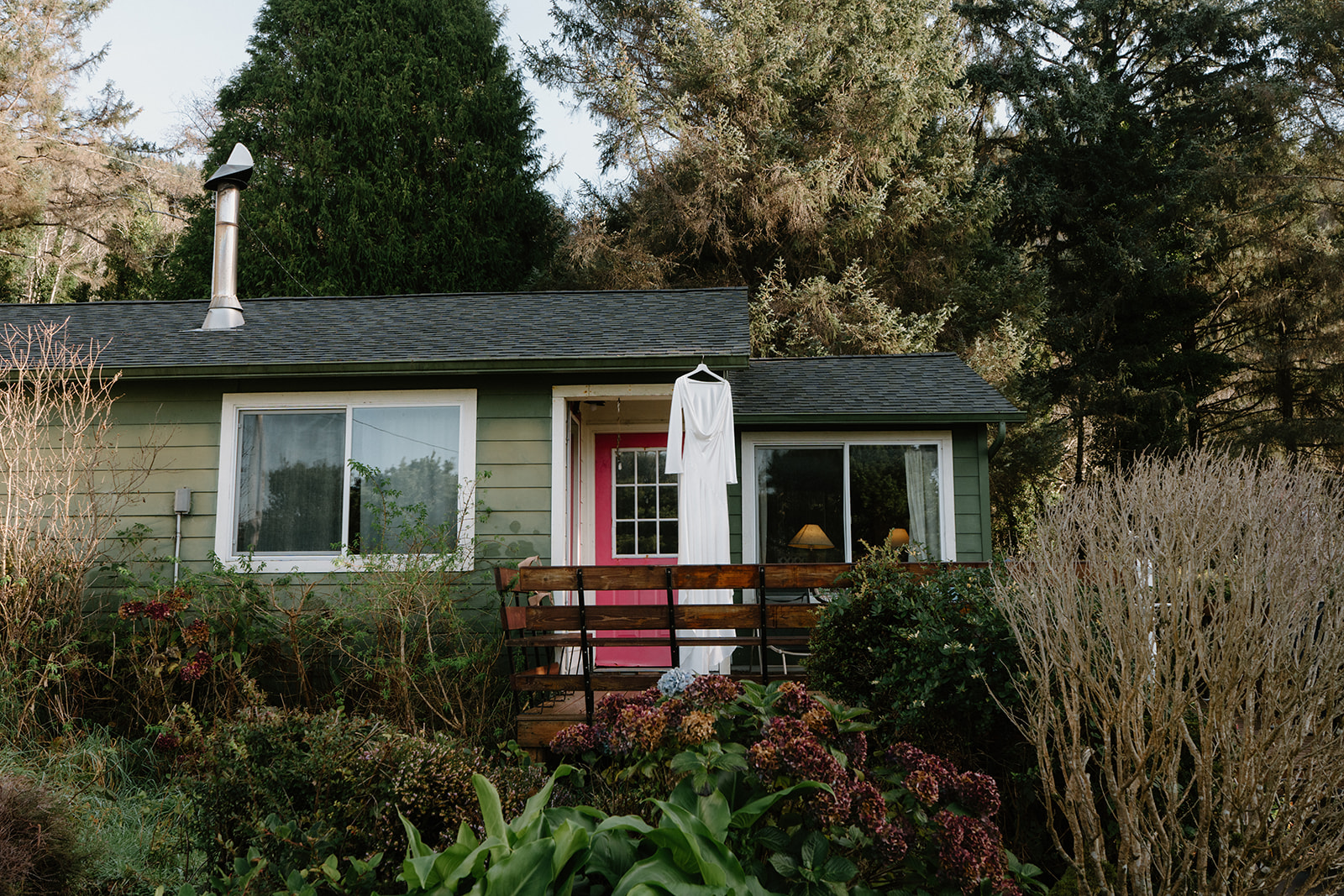 A cozy Airbnb with a lush garden in front of it and a wedding dress hanging on the patio. Taken for a Florence, Oregon elopement.