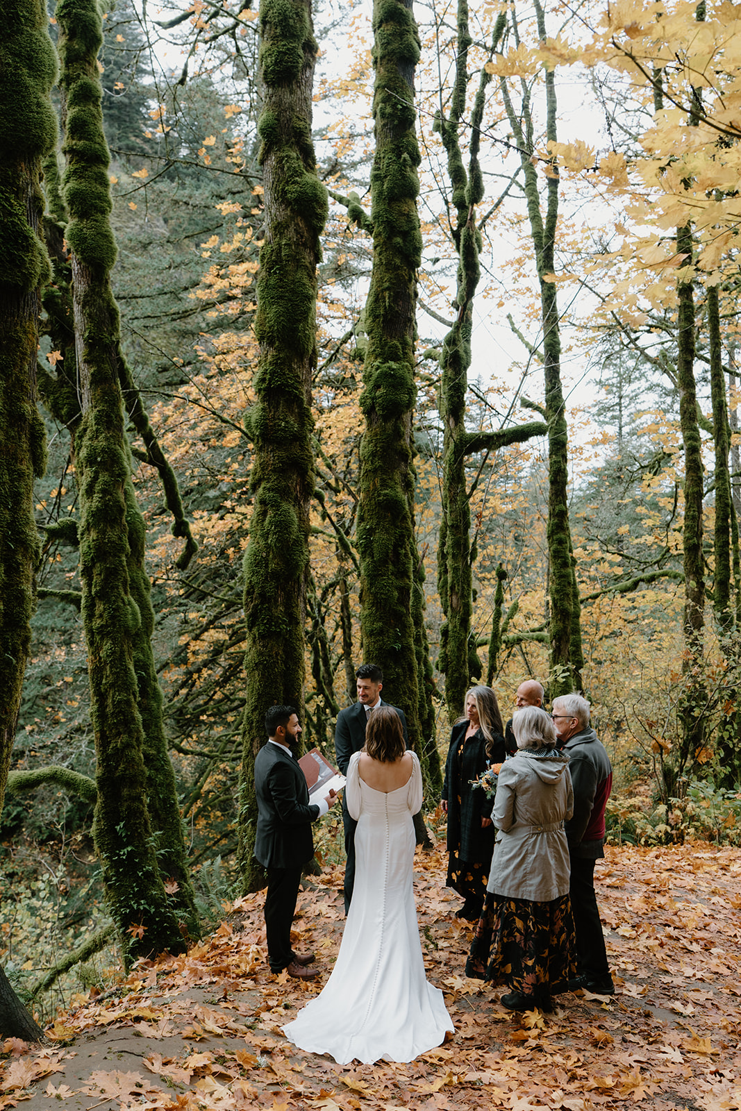 A small group of people huddle around a bride and groom in the woods during their Latourell Falls elopement.