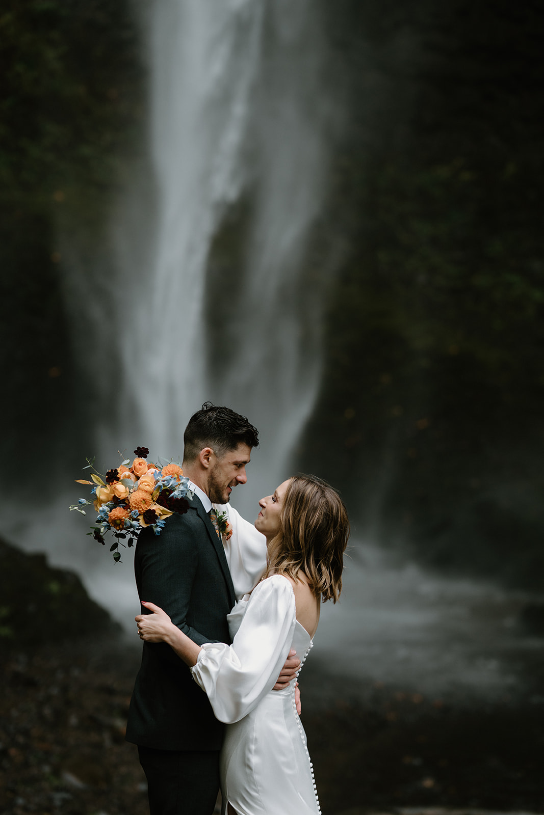 A close up photo of a couple in wedding attire standing in front of a waterfall during their Latourell Falls elopement.