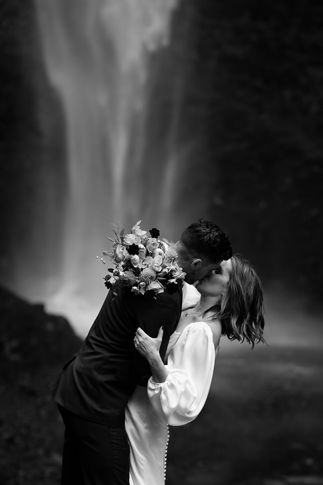 A black and white photo of a couple dramatically kissing in front of a waterfall during their Latourell Falls elopement.