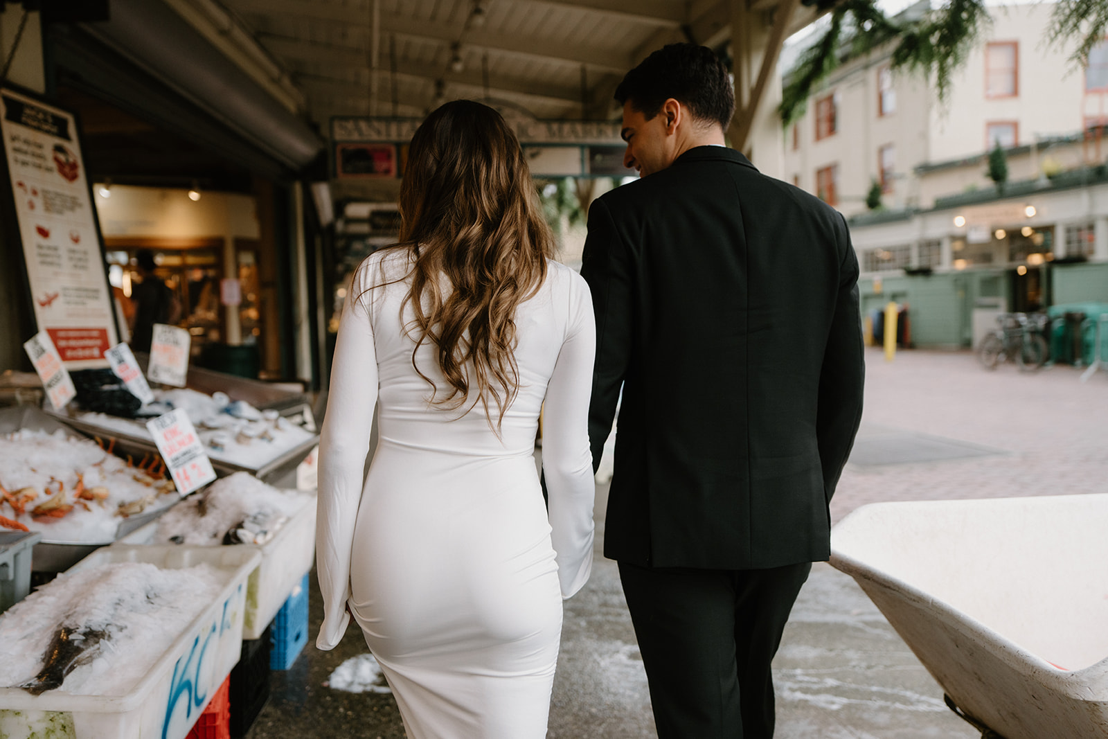 A couple in wedding attire holds hands and walks together looking at fish during their Pike Place elopement. 
