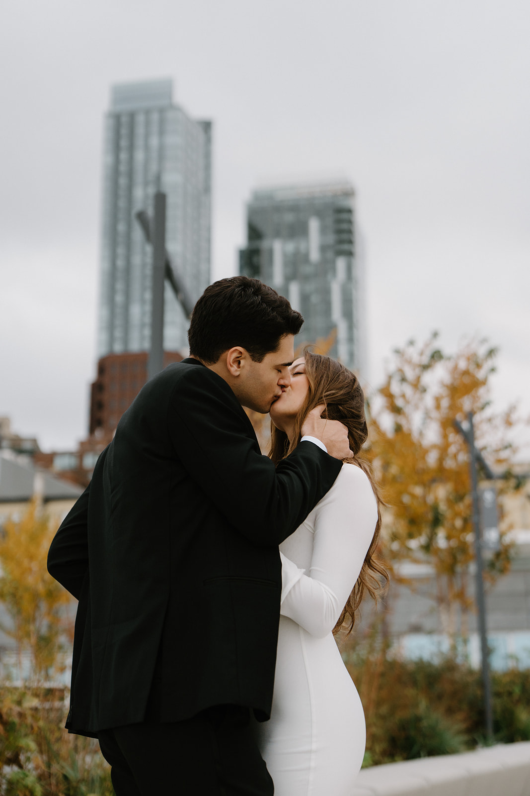 A couple kisses in front of changing leaves and tall buildings in Seattle during their Pike Place elopement. 