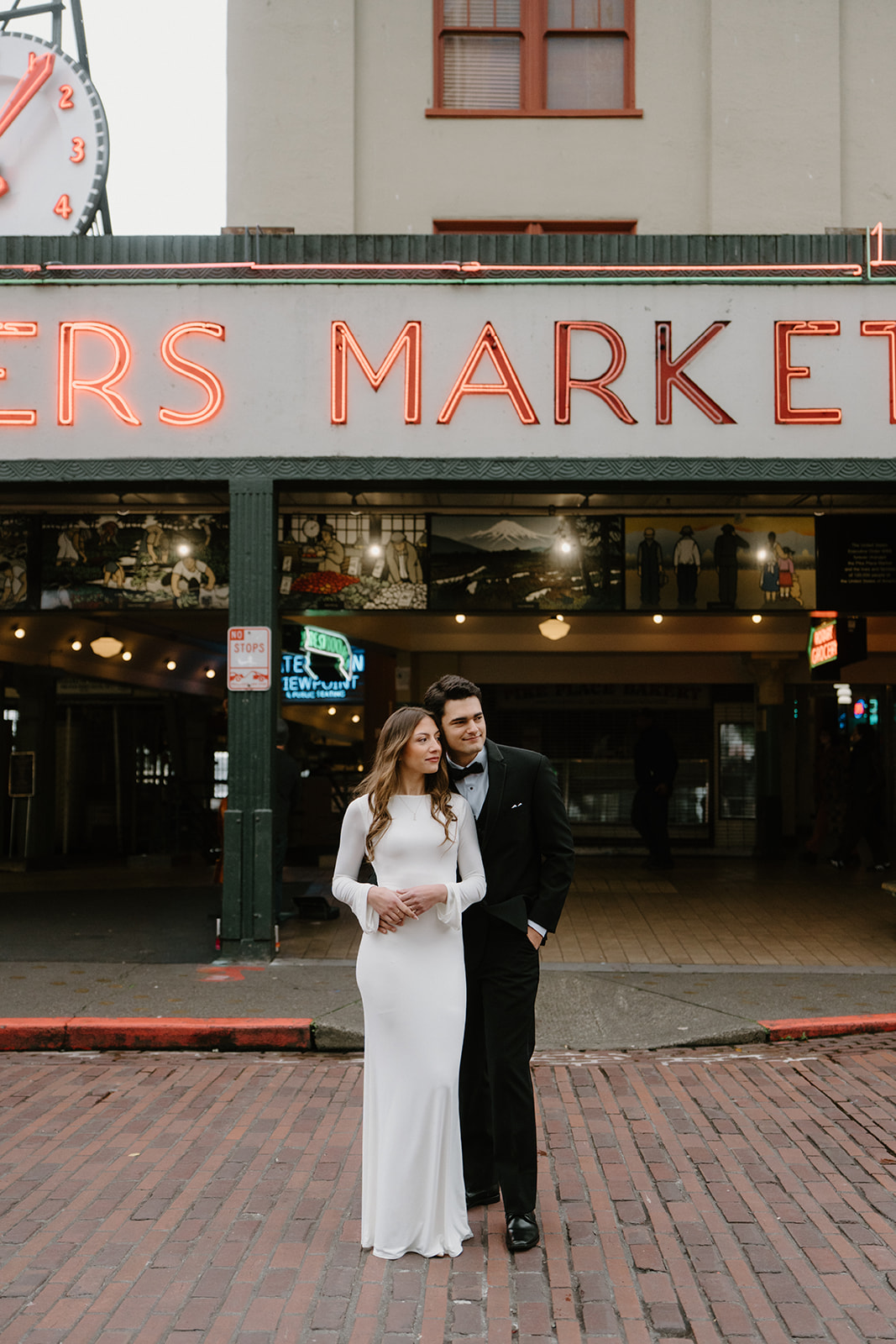 A couple in wedding attire stands in front of the Pike Place Market sign in Seattle. 