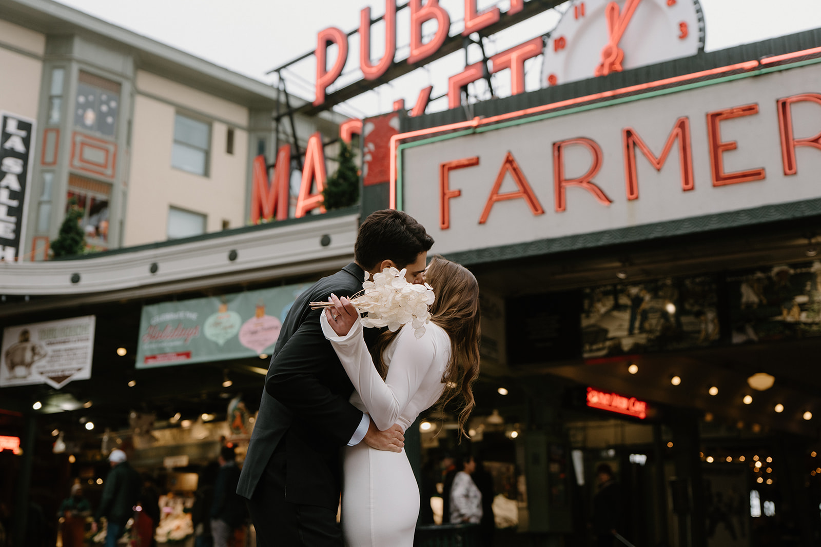 A couple embraces and kisses in front of the Pike Place Market sign during their elopement. 
