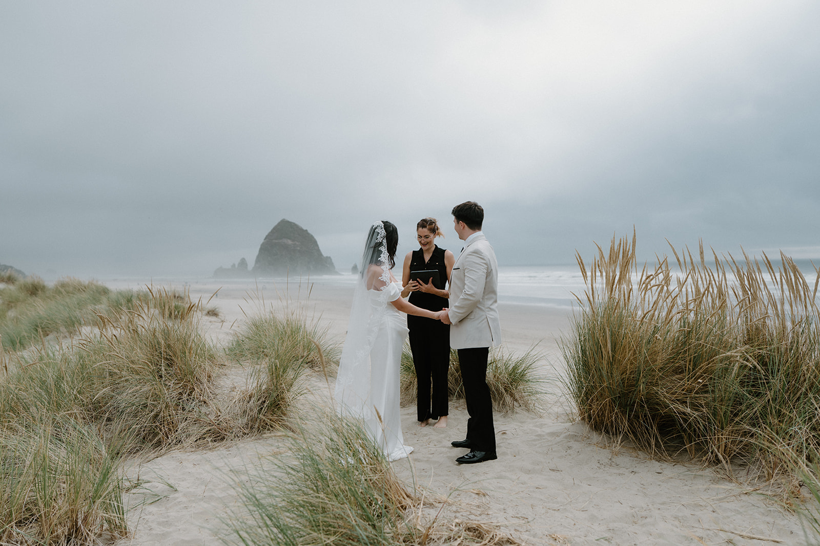 A couple exchanges wedding vows with an officiant in front of Haystack Rock during their Oregon Coast elopement. 