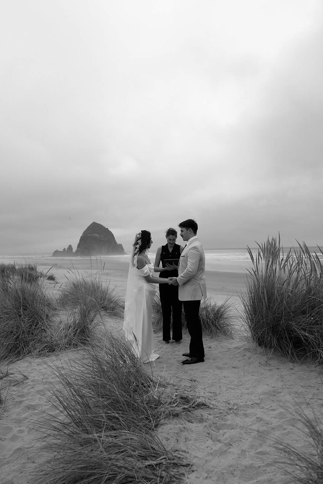 A couple exchanges wedding vows with an officiant in front of Haystack Rock during their Oregon Coast elopement. 
