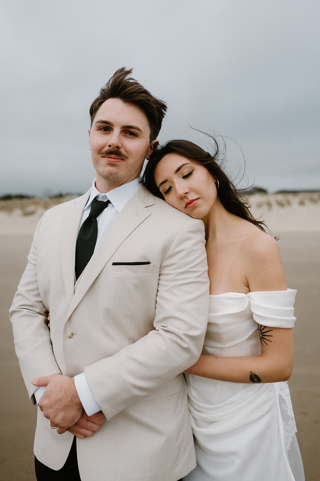 A portrait of a couple in wedding attire standing on the beach and looking at the camera during their Oregon Coast elopement. 
