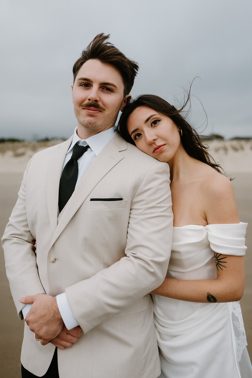 A portrait of a couple in wedding attire standing on the beach and looking at the camera during their Oregon Coast elopement. 