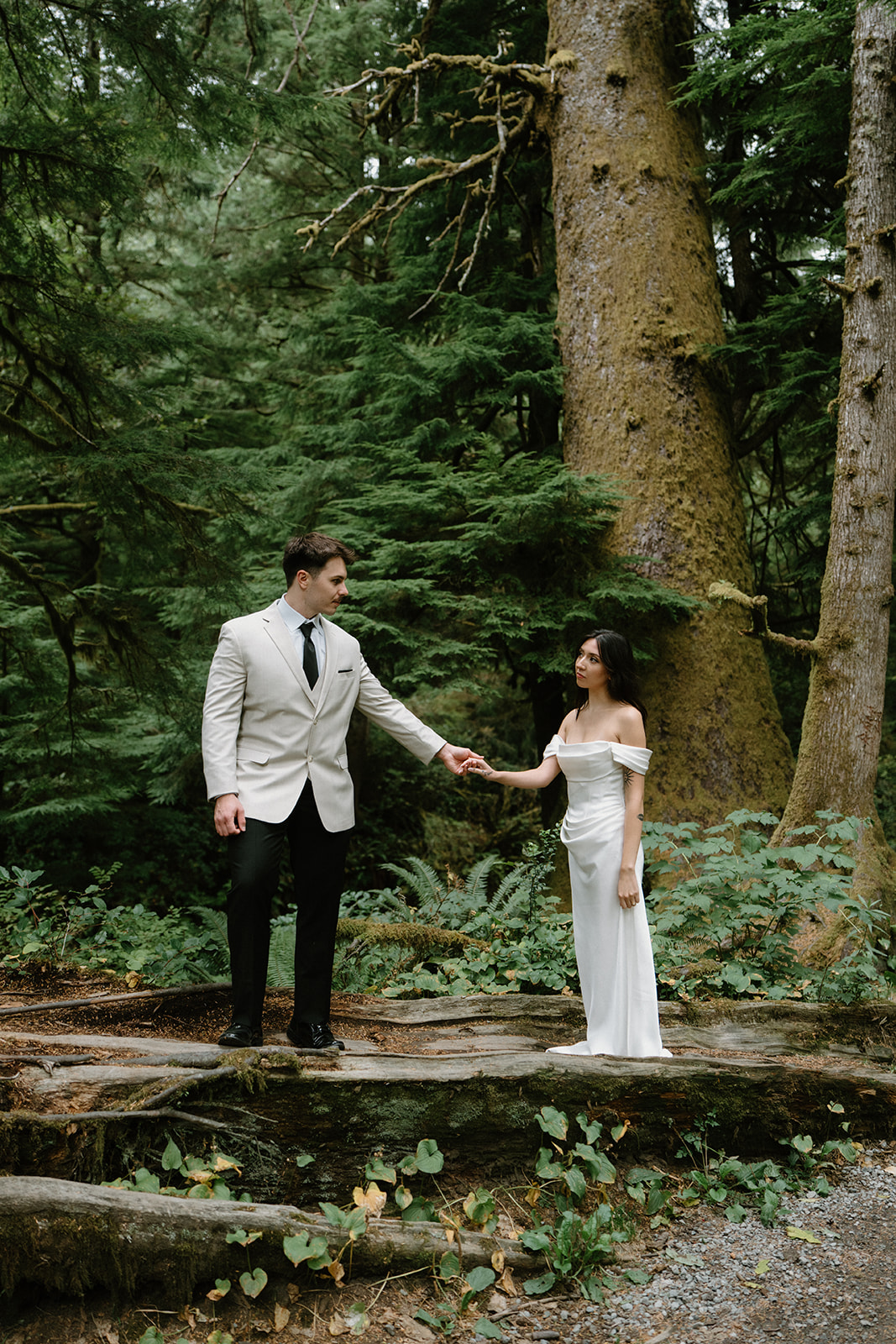 A couple stands in a dark green forest in wedding attire during their Oregon Coast elopement. 