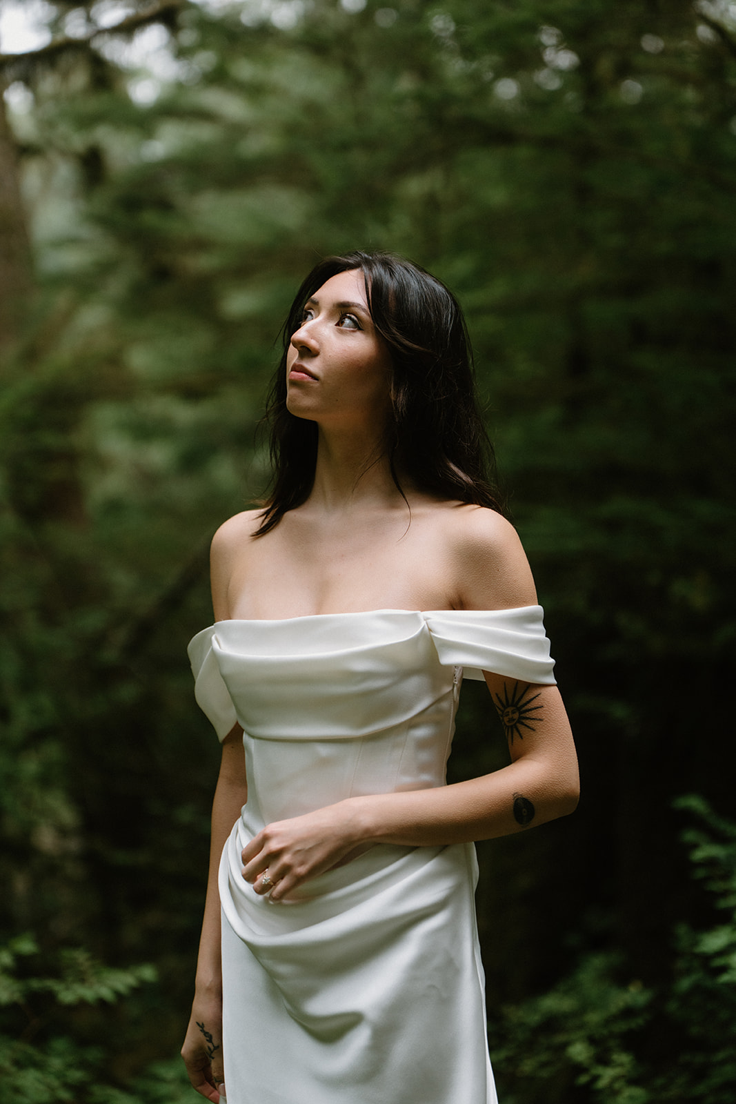 A bride stands in the forest and looks towards the light during her Oregon Coast elopement. 