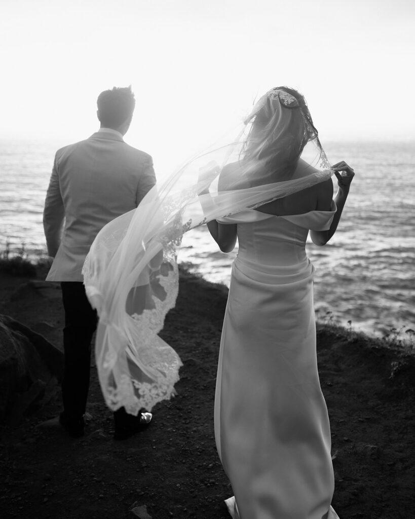 A black and white photo of a couple standing on a windy cliff during an Oregon coast elopement. 
