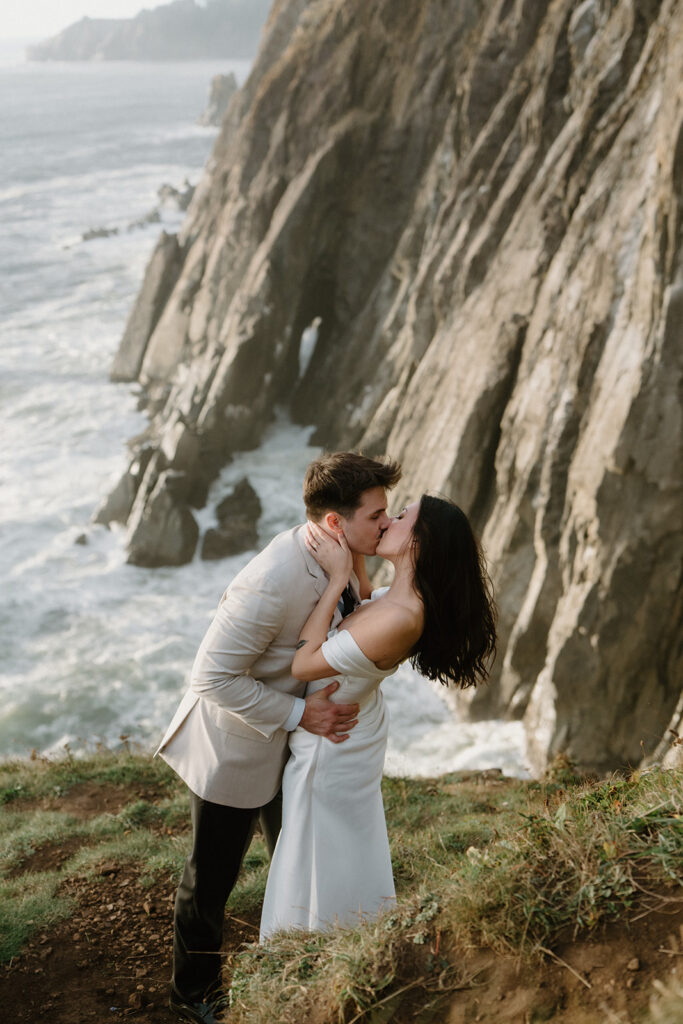 A couple kisses dramatically on a cliff during an Oregon coast elopement. 
