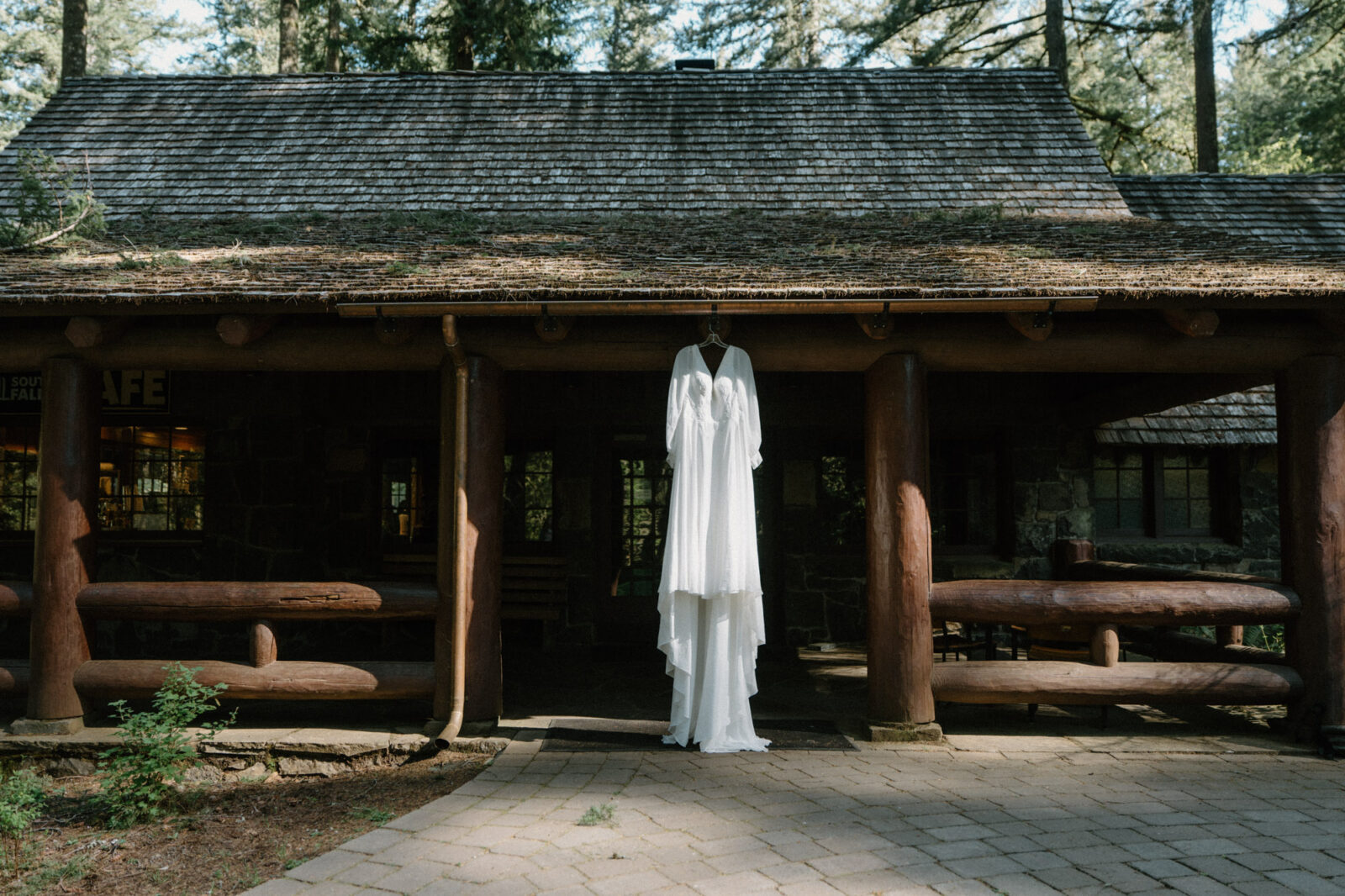 A white dress hangs in front of a log cabin at a Silver Falls elopement. 