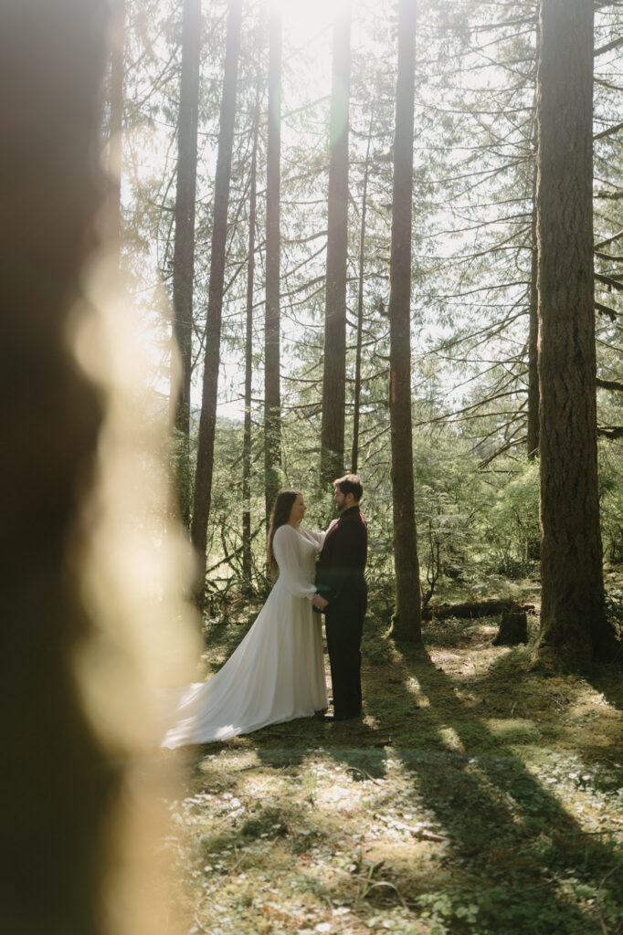 A couple stands in a patch of light in the woods at a Silver Falls elopement