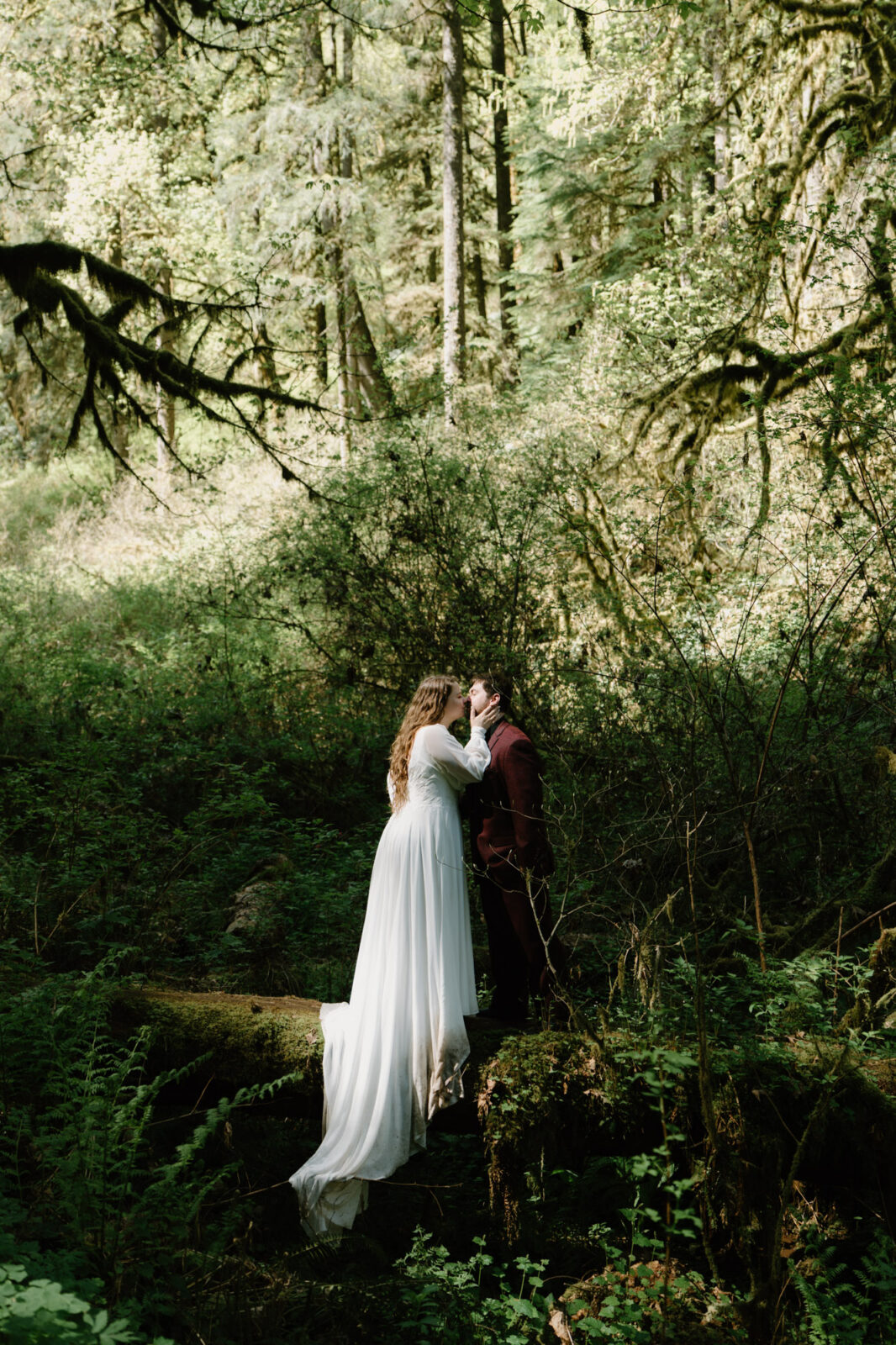 A couple stands on a log in the woods and kisses at a Silver Falls elopement