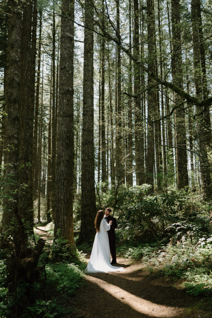 A couple stands in a patch of light in the woods at a Silver Falls elopement