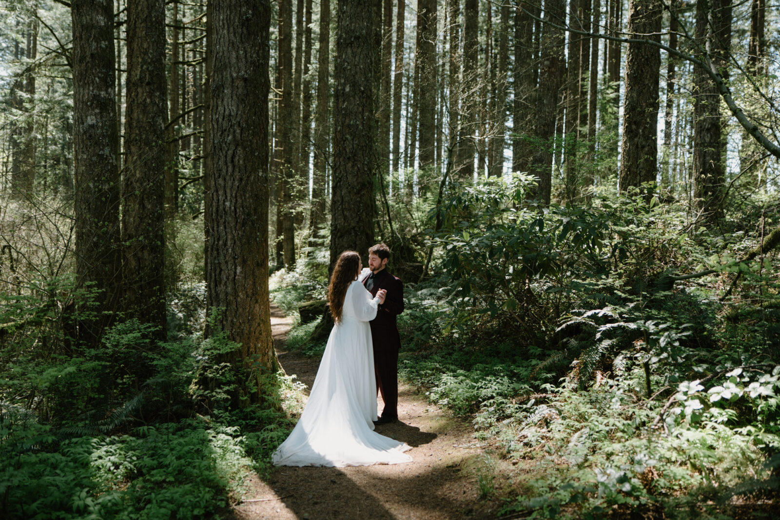 A couple stands in a patch of light in the woods at a Silver Falls elopement
