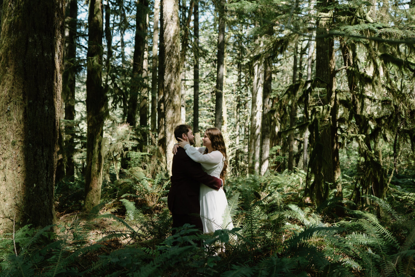 A couple stands in a patch of woodsy ferns and kisses during a Silver Falls elopement. 