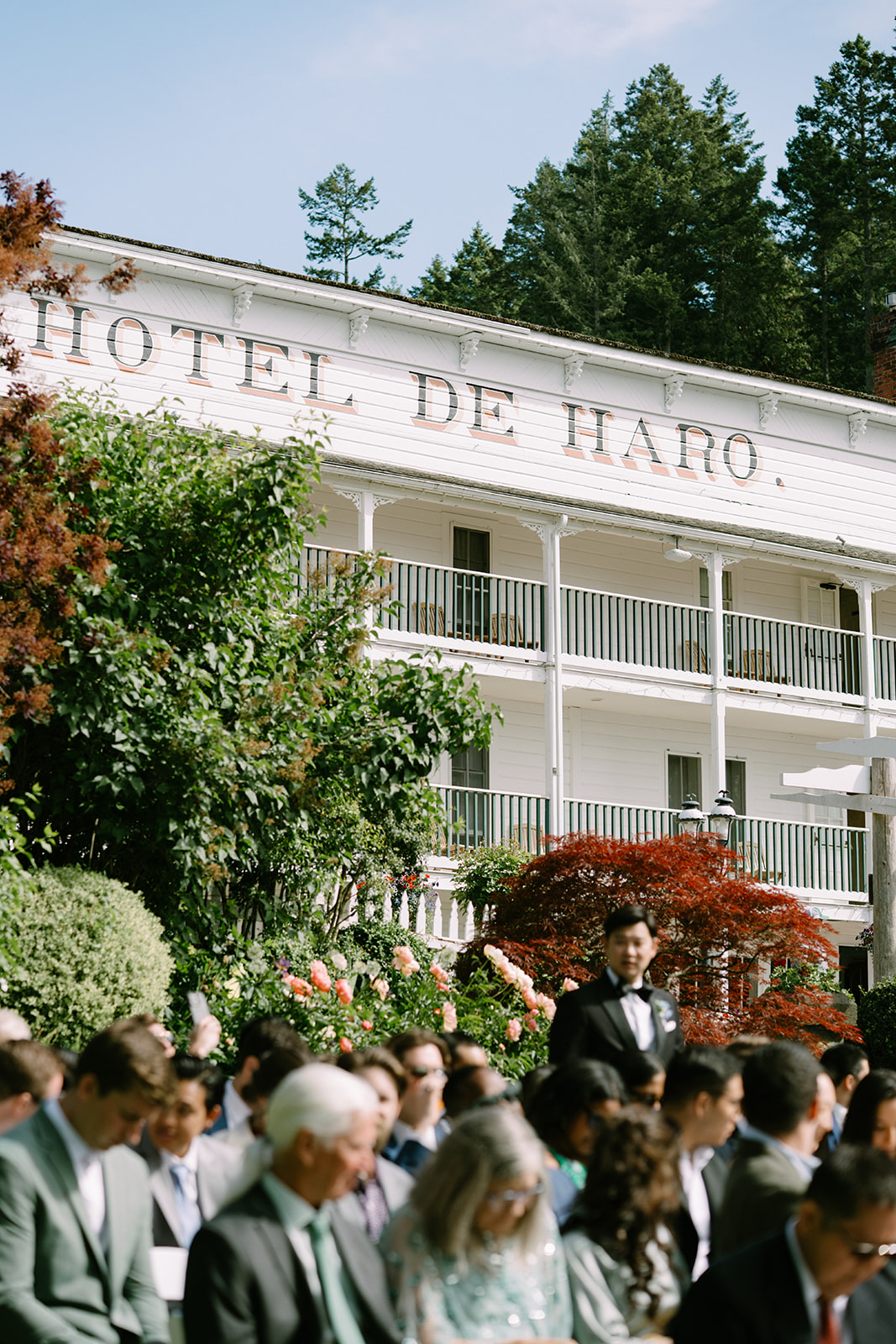 The Roche Harbor Resort garden ceremony space set up for an intimate outdoor wedding on San Juan Island, Washington. Pink peonies in bloom and guests gathering under the summer sky.
