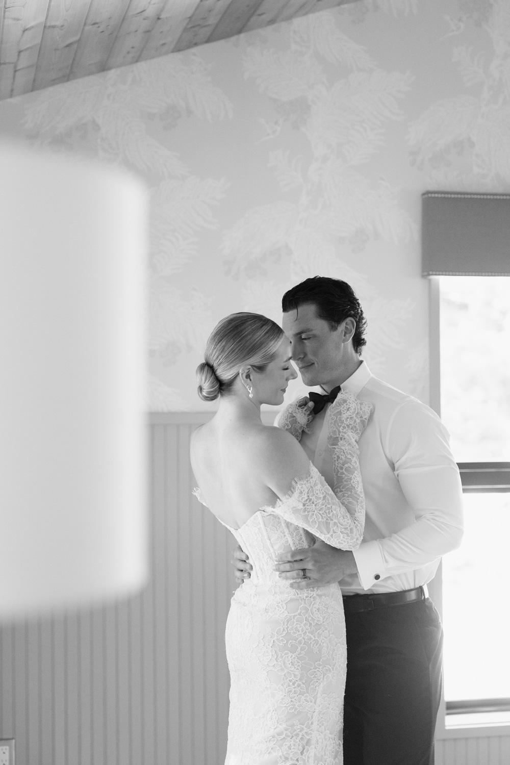 A black and white photo of a couple in wedding attire, helping each other get ready at the Carly Estate wedding venue.