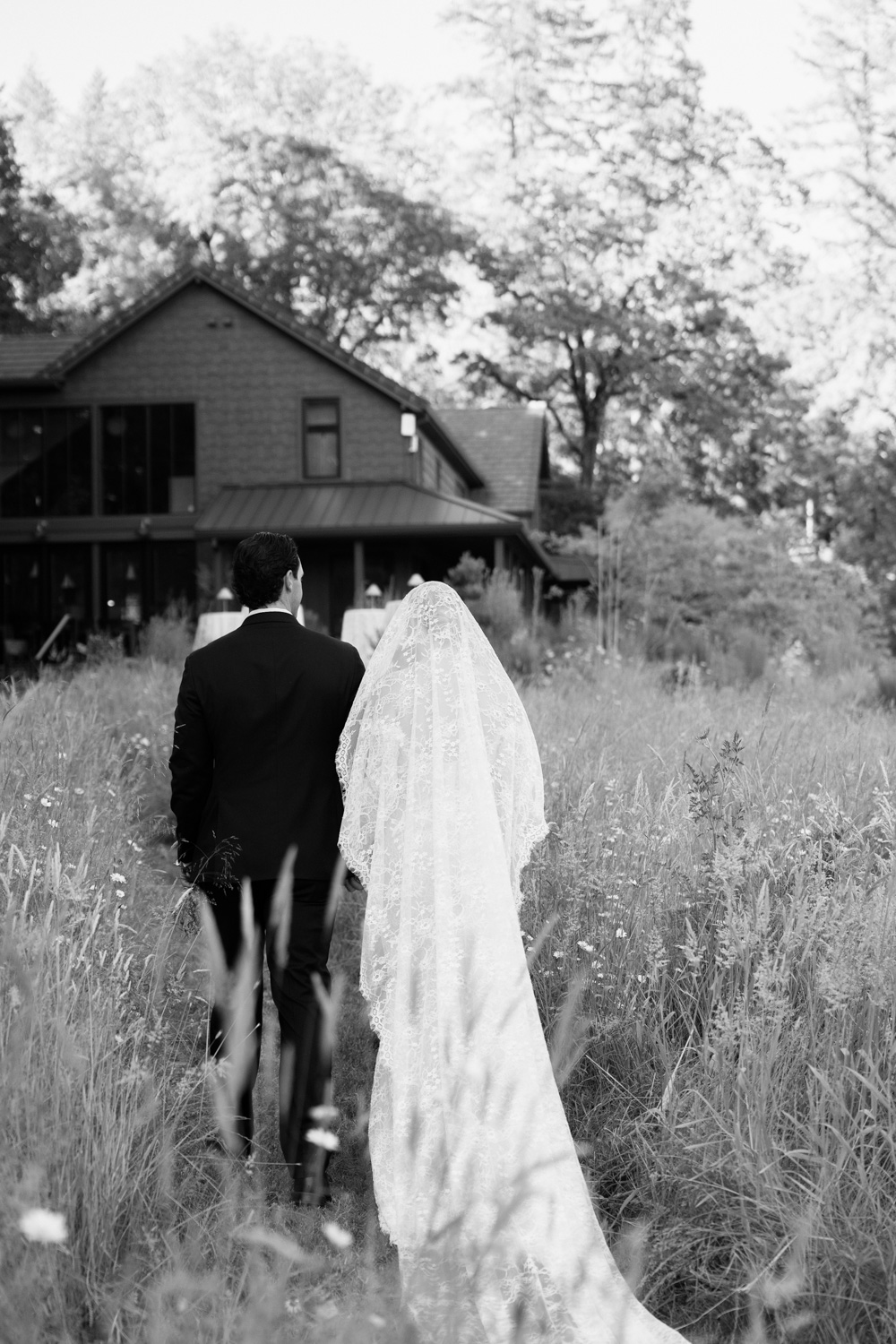 A black and white photo of a bride and groom walking towards the Carly Estate after their wedding photos.