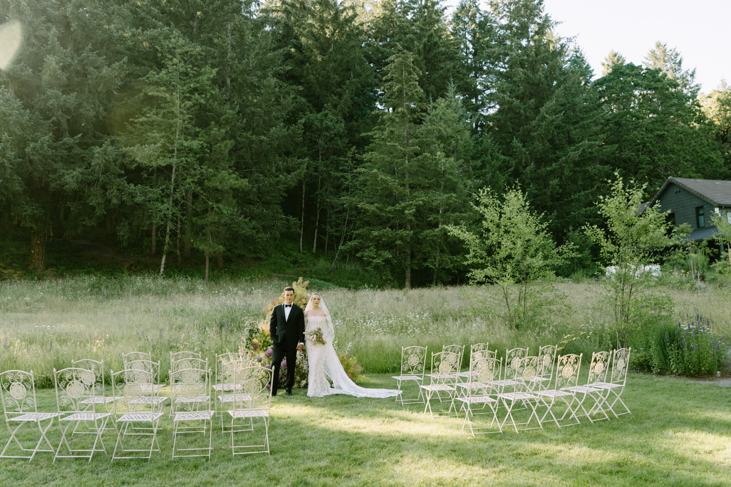 A couple stands hand in hand in golden light in a field at their Carly Estate Wedding.