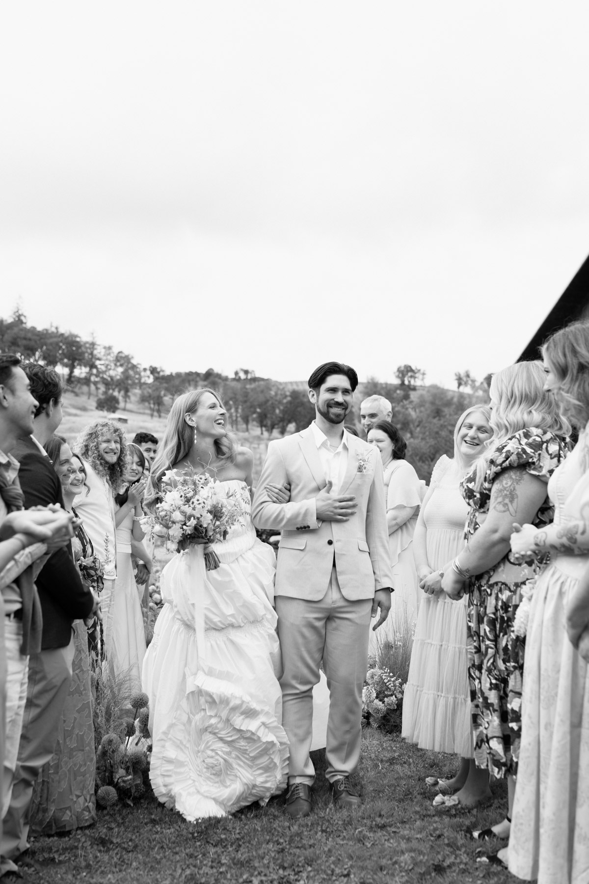 A black and white photo of a couple walking into their wedding ceremony surrounded by guests at Maysara Winery