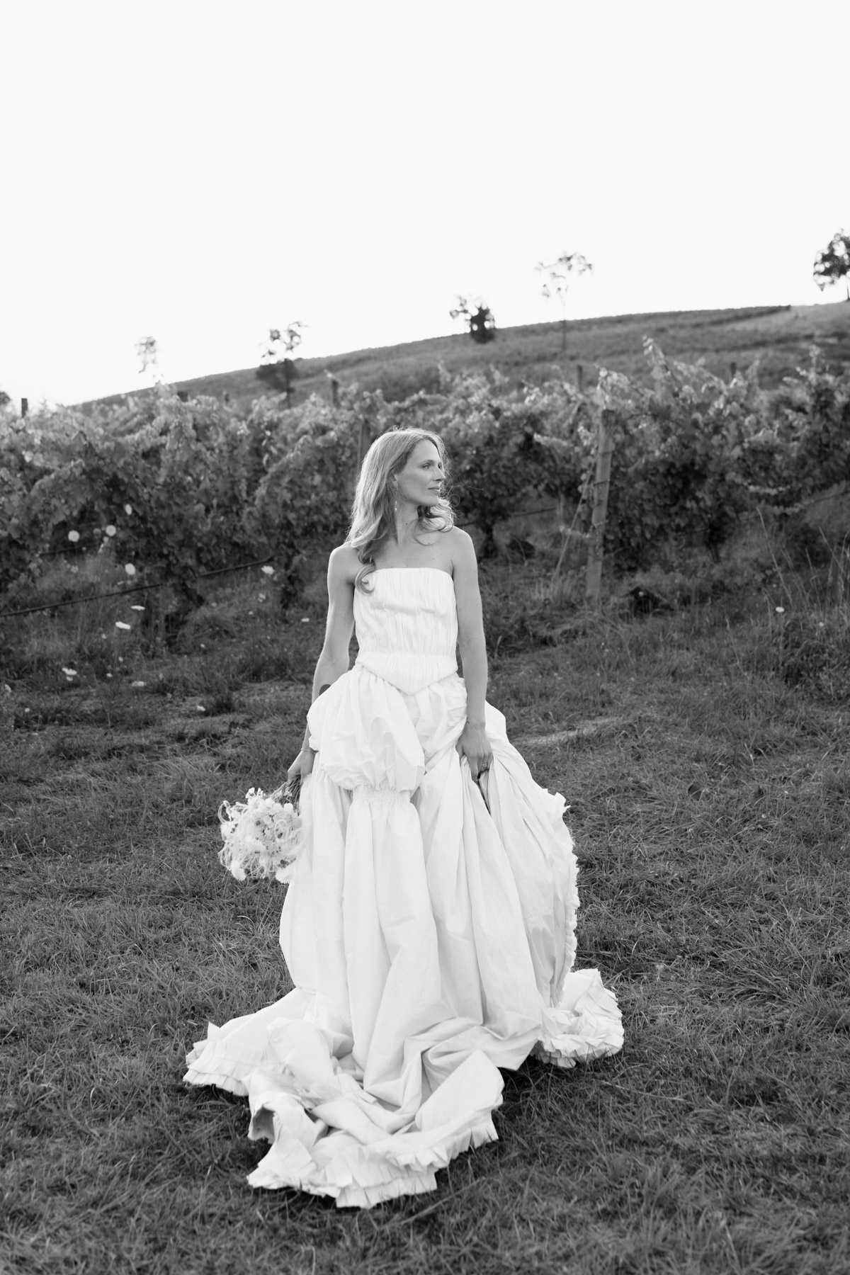 A black and white photo of a bride standing in a vineyard after her wedding at Maysara Winery