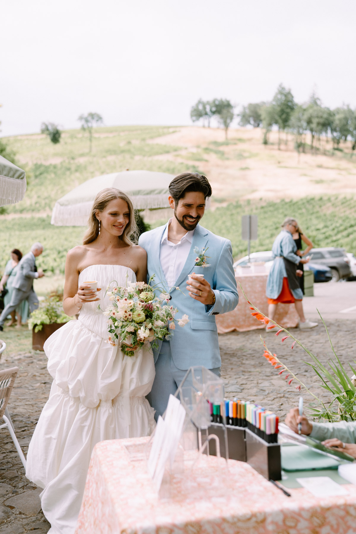 A couple in wedding attire stands and watches a painter painting their portrait at a wedding at Maysara Winery