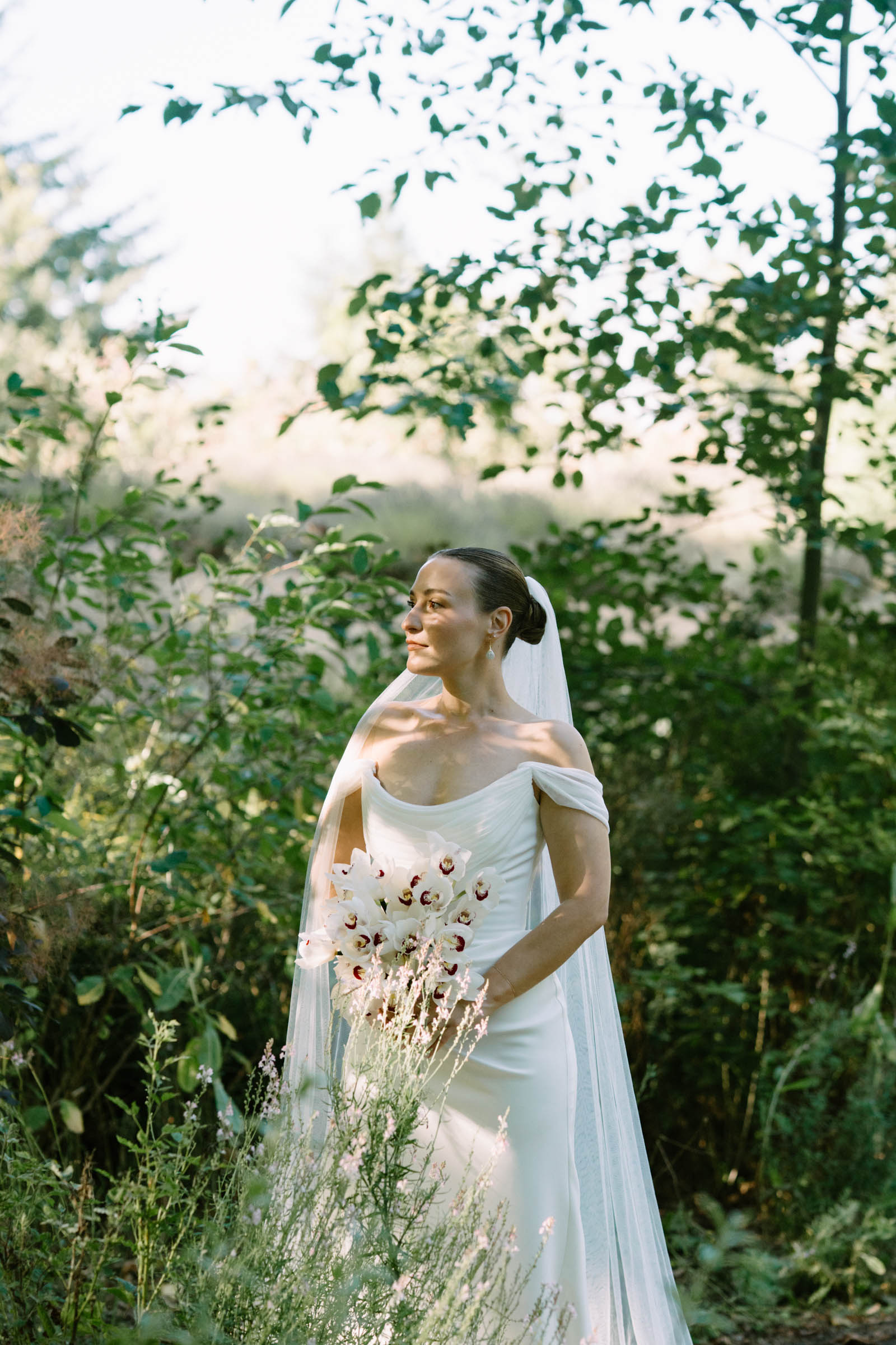 Partner in a gown and veil holding a bouquet among tall garden greenery at Anker Place