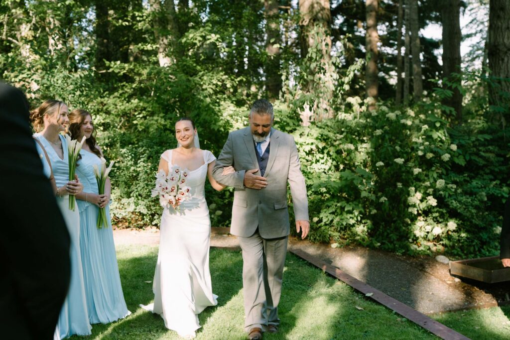 Wedding processional at Anker Place, the couple walking in arm in arm past guests and tall evergreens