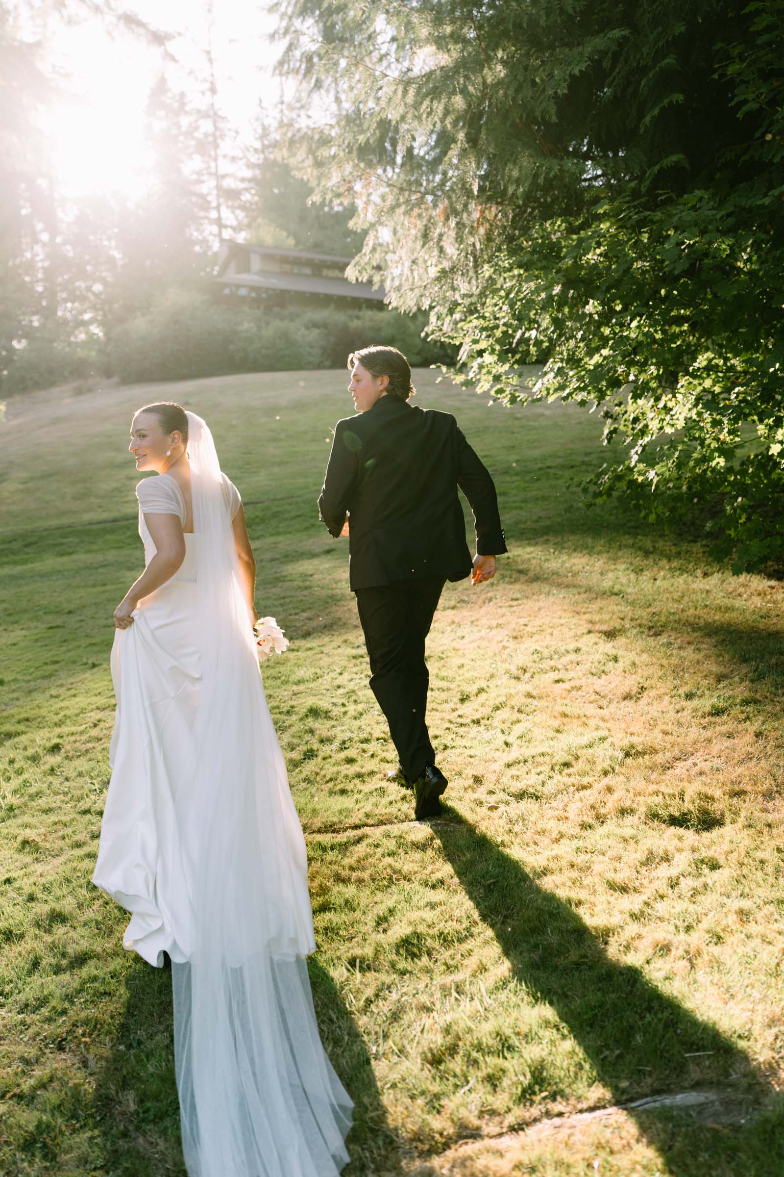 Couple walking a sunlit lawn at Anker Place at golden hour, gown train on the grass