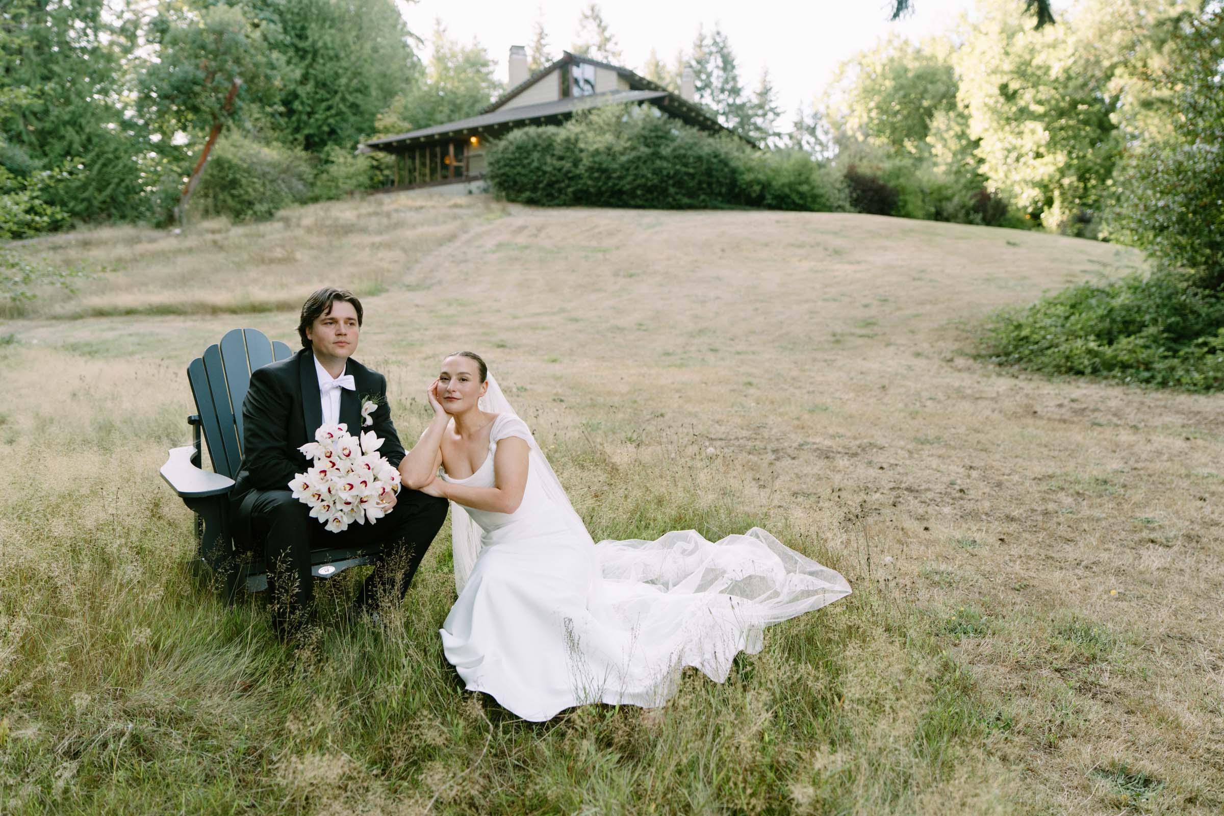 Couple seated together on a sofa out in the meadow grass at Anker Place, one holding a bouquet