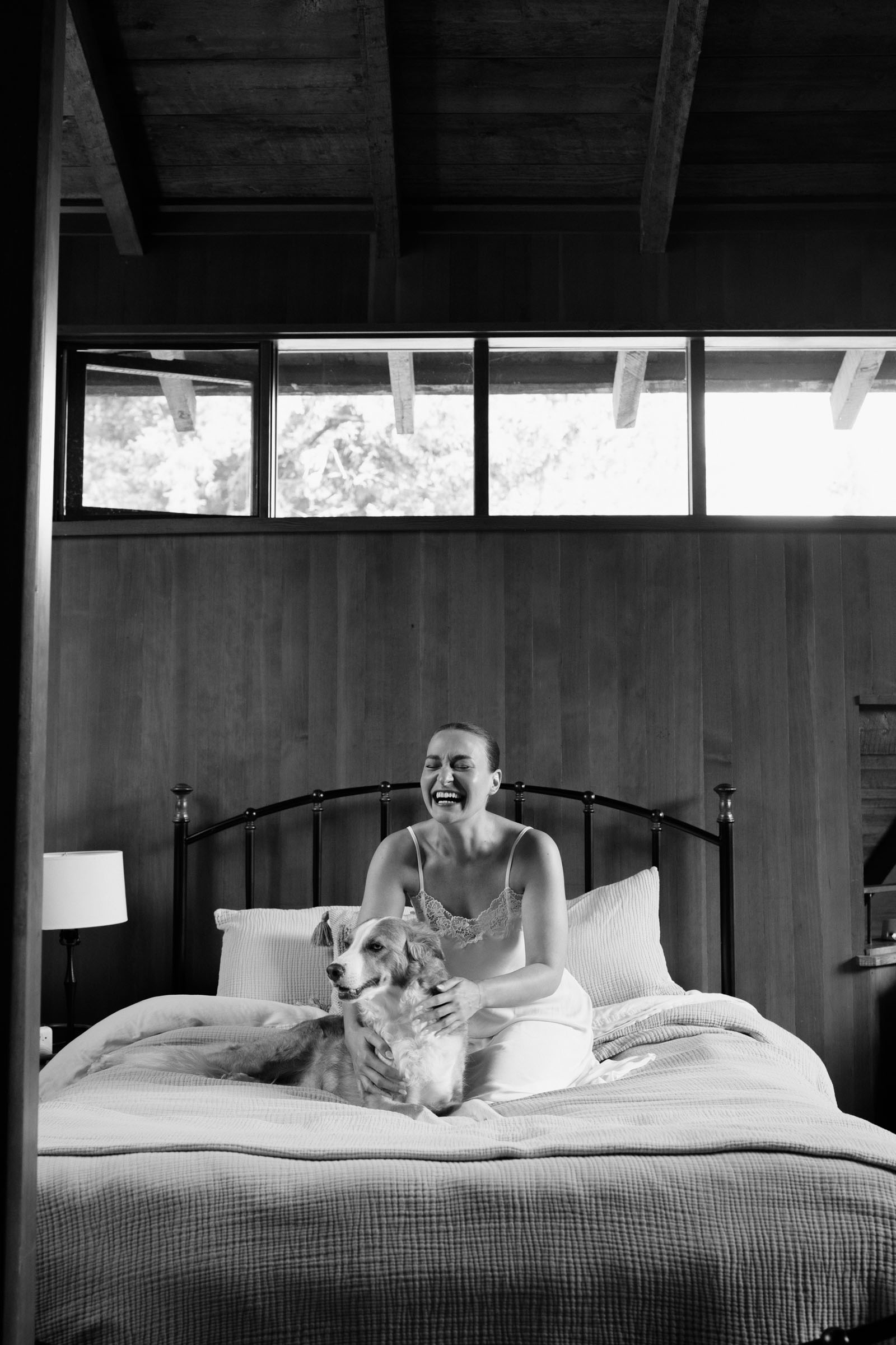 Partner laughing on the bed with their dog while getting ready at Anker Place, under the mid-century clerestory windows