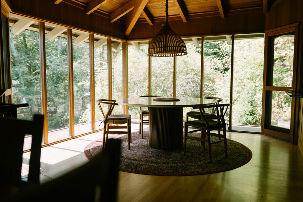 Mid-century dining room inside Anker Place, the former Kingston House, with a wood-beamed ceiling, cane-back chairs, and tall windows