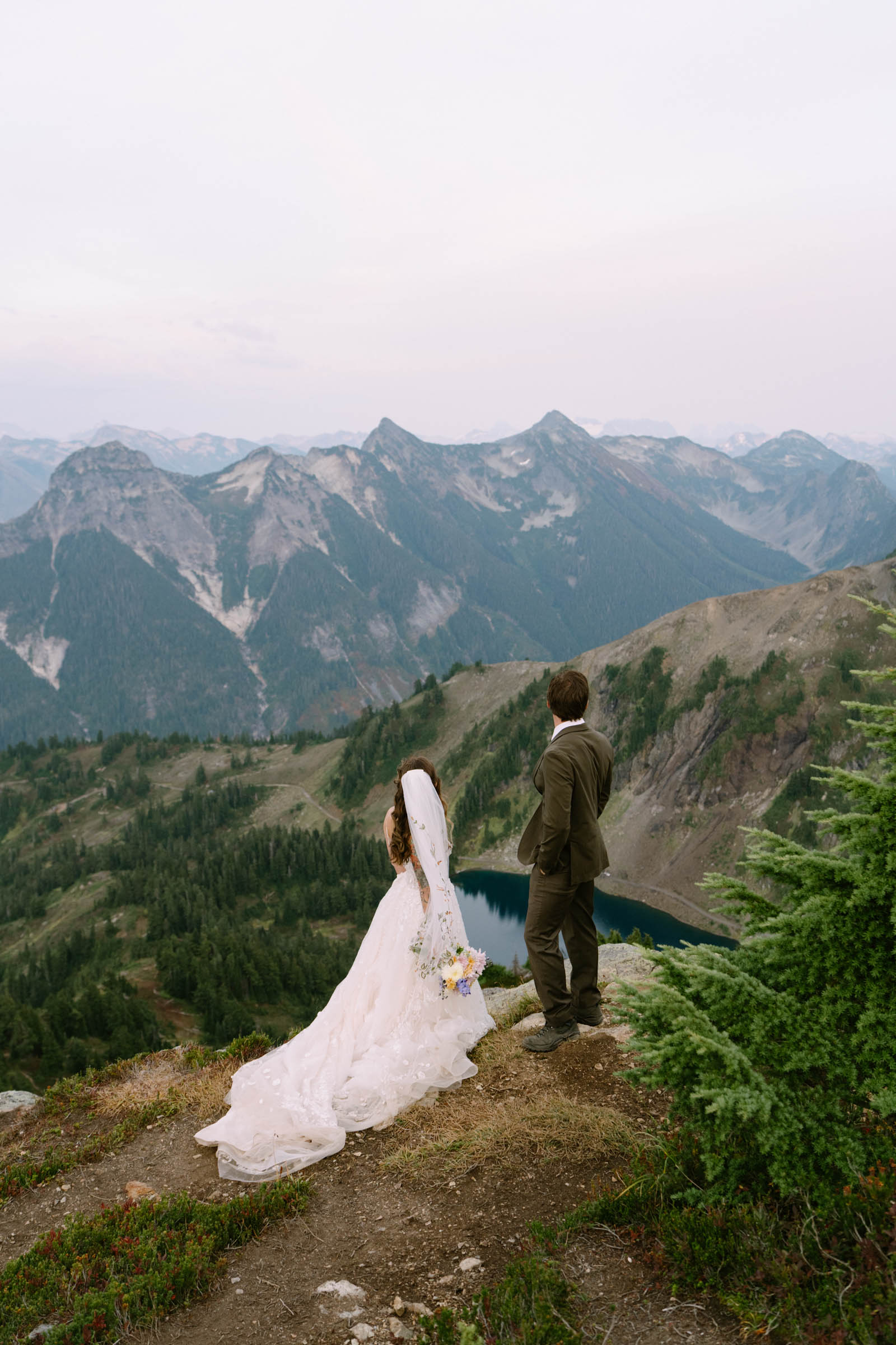 Couple in elopement attire on a ridge with North Cascades peaks behind them