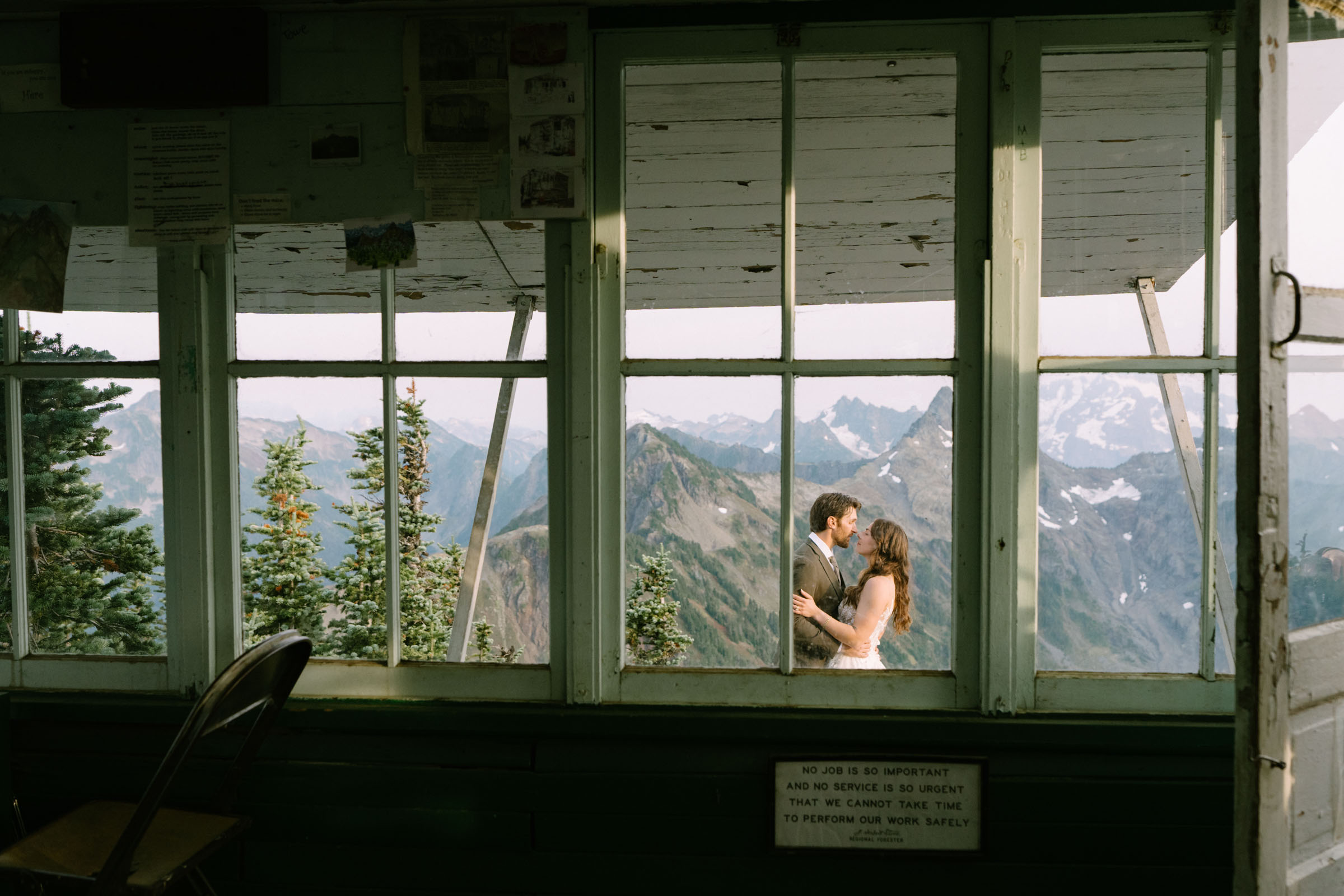 Couple holding each other inside the Winchester Mountain fire lookout, forest framed in the windows