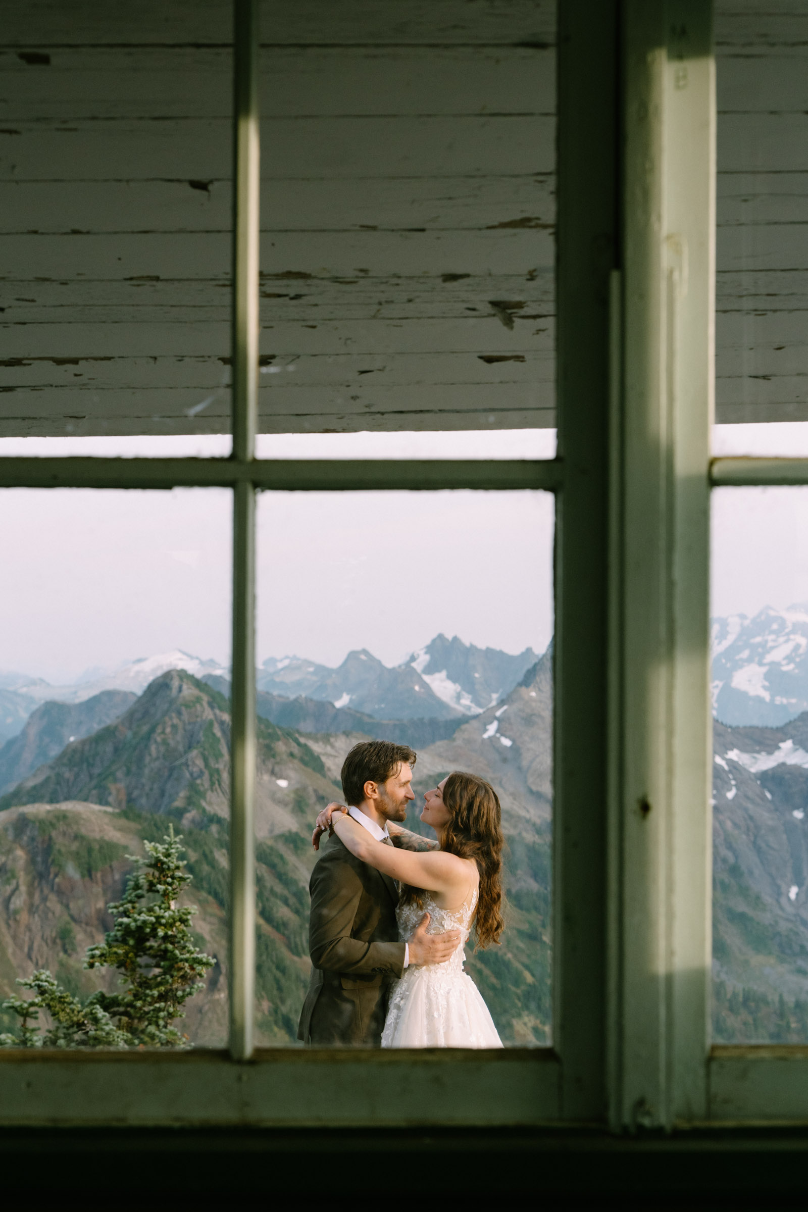 Couple embracing framed in a lookout window, mountains reflected in the glass